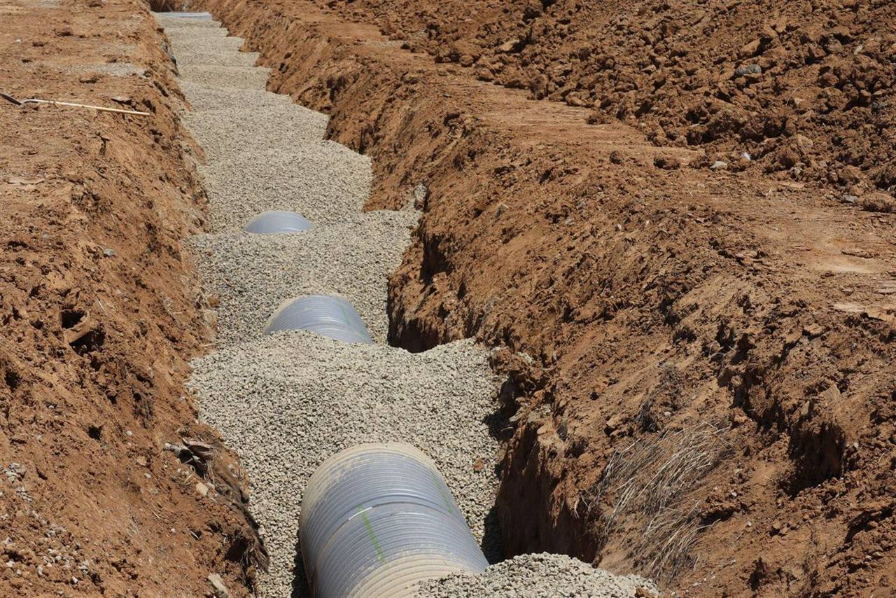 Newly laid drainage pipe bedded in gravel in an excavated trench