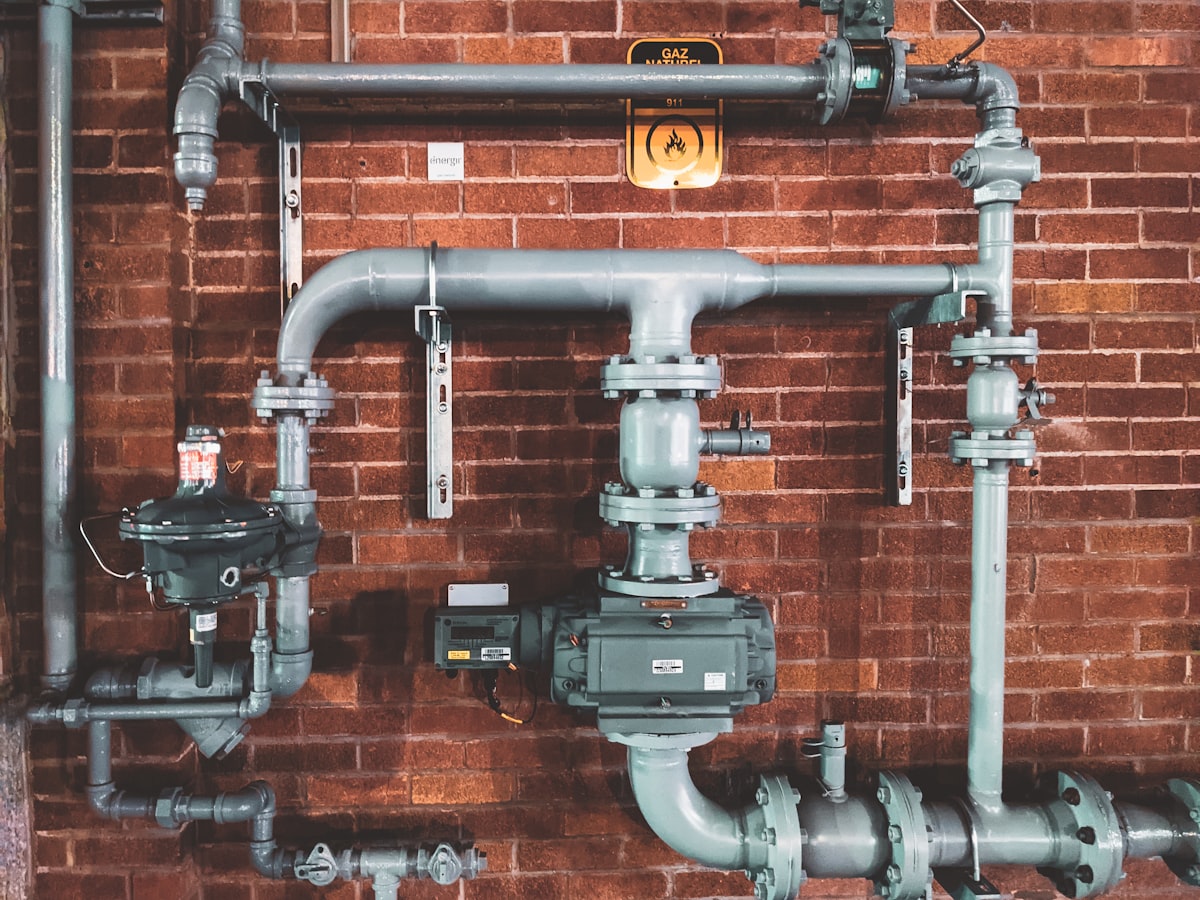 Commercial plant-room pipework with valves against a brick wall