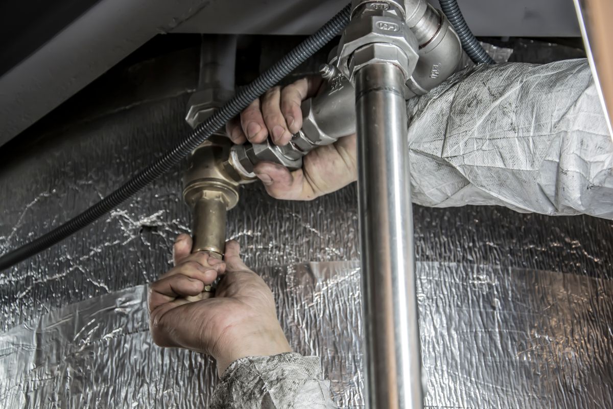 Plumber fitting chrome waste pipework under a unit