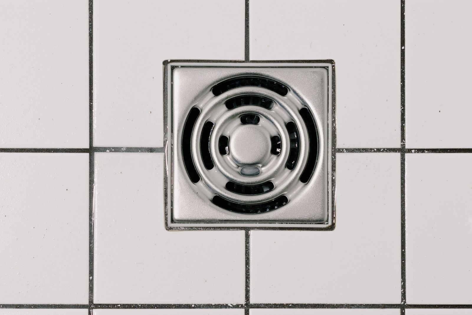 Stainless-steel shower floor drain set into white tiling