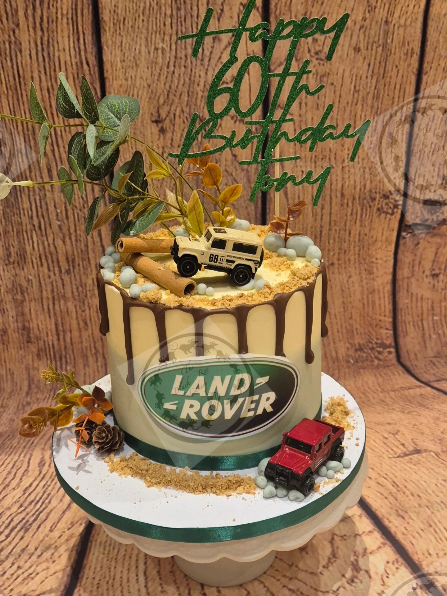 White chocolate drip cake with a miniature Land Rover Defender model, cinnamon sticks and dried foliage for a 60th birthday