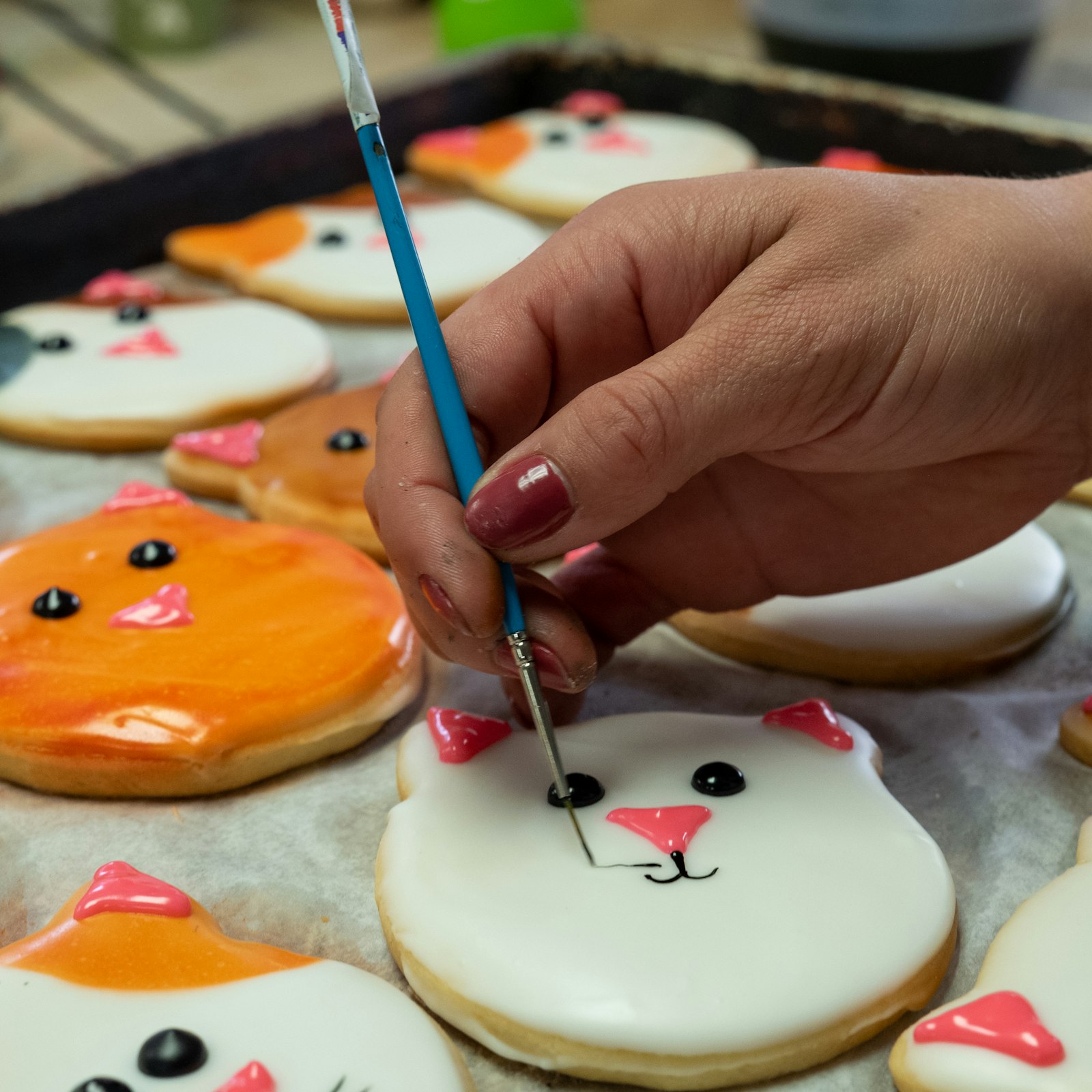 Hands using decorating tools to ice a batch of cookies