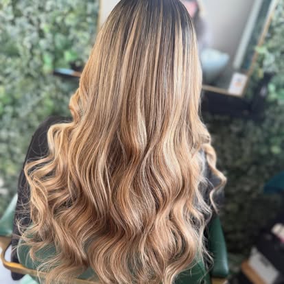 Long balayage hair with soft caramel-to-blonde graduation, styled in loose waves