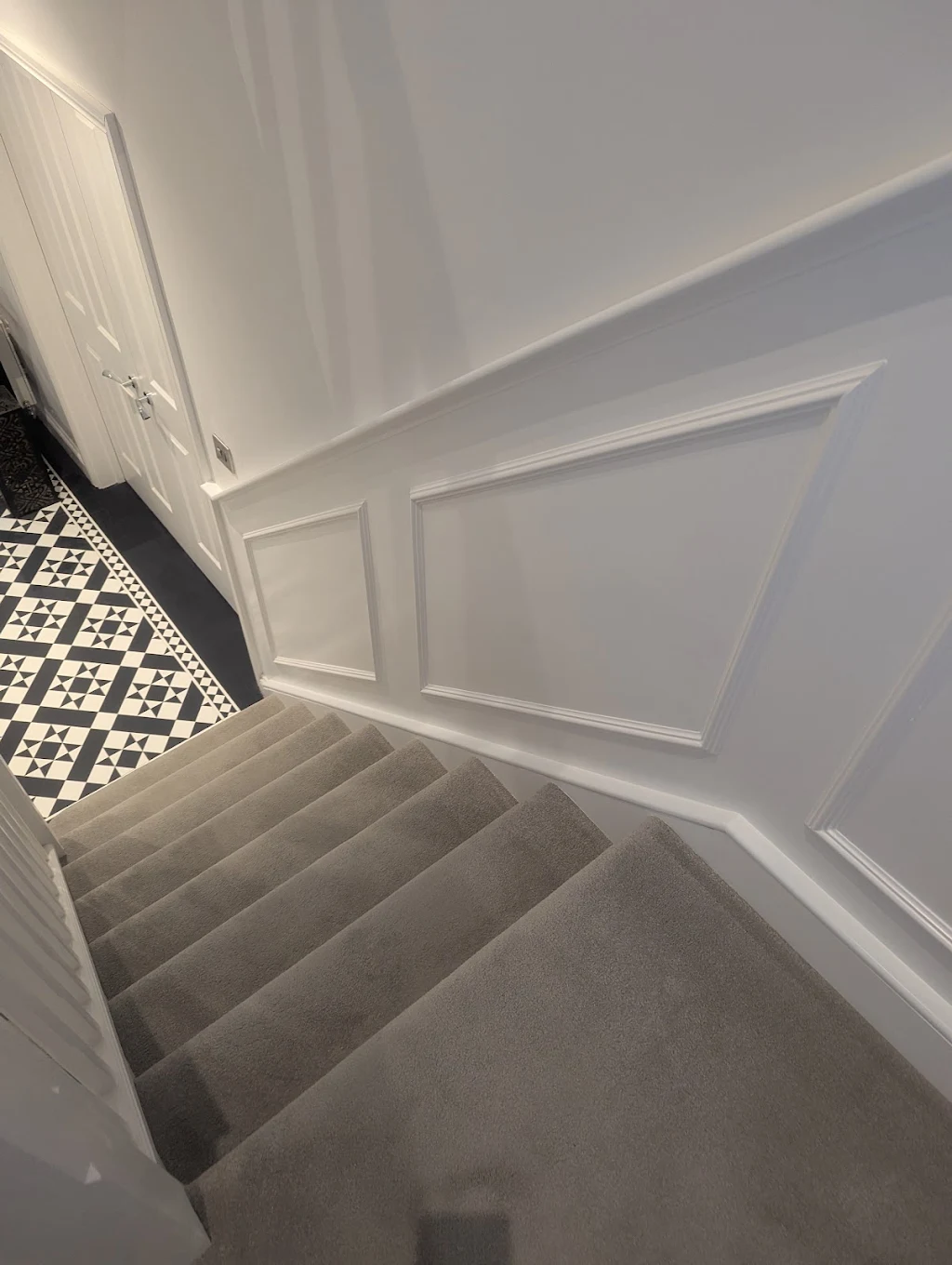 Freshly painted staircase and wall panelling above a Victorian-tiled hallway