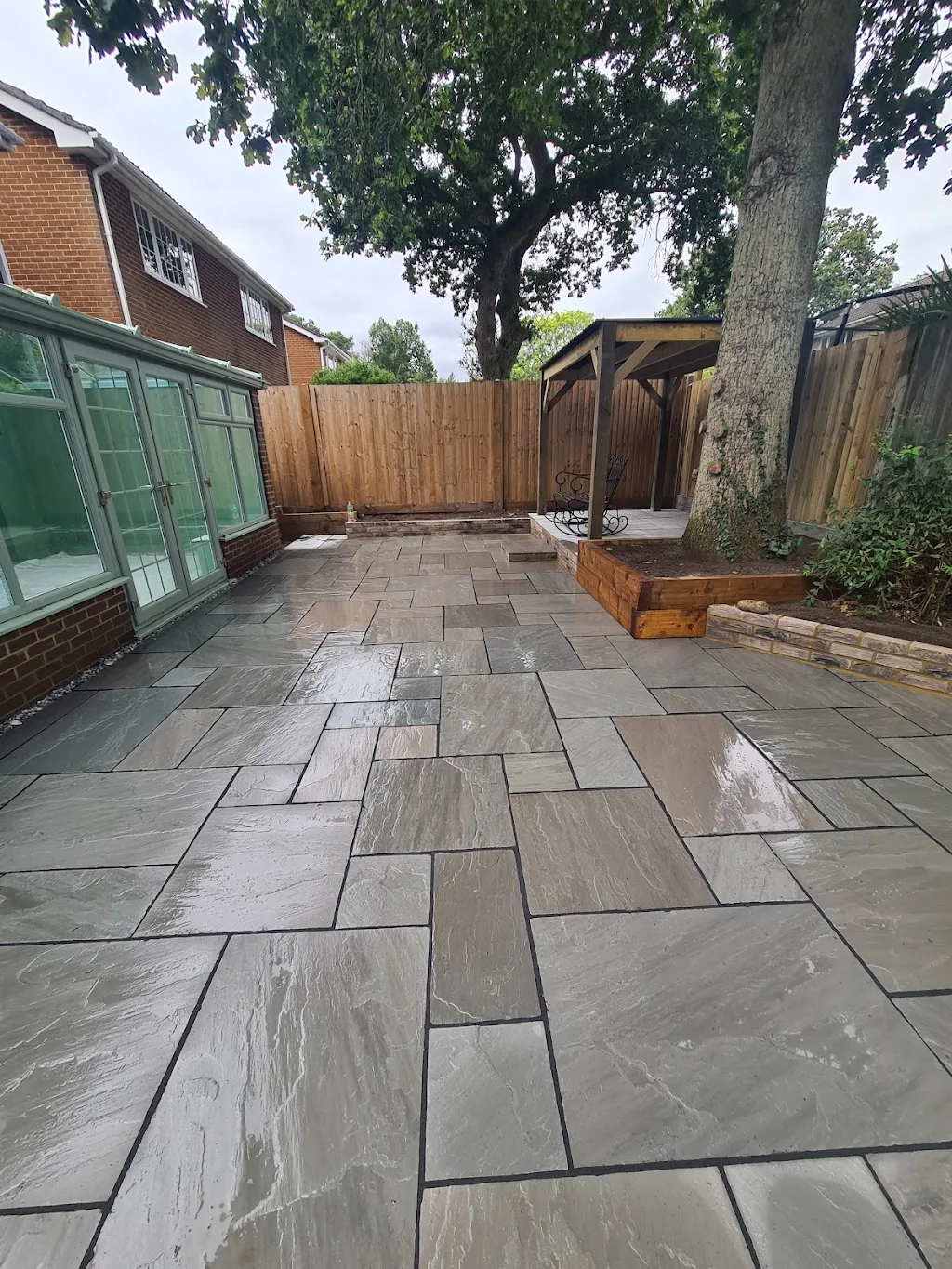 Grey stone patio with timber pergola beside a conservatory