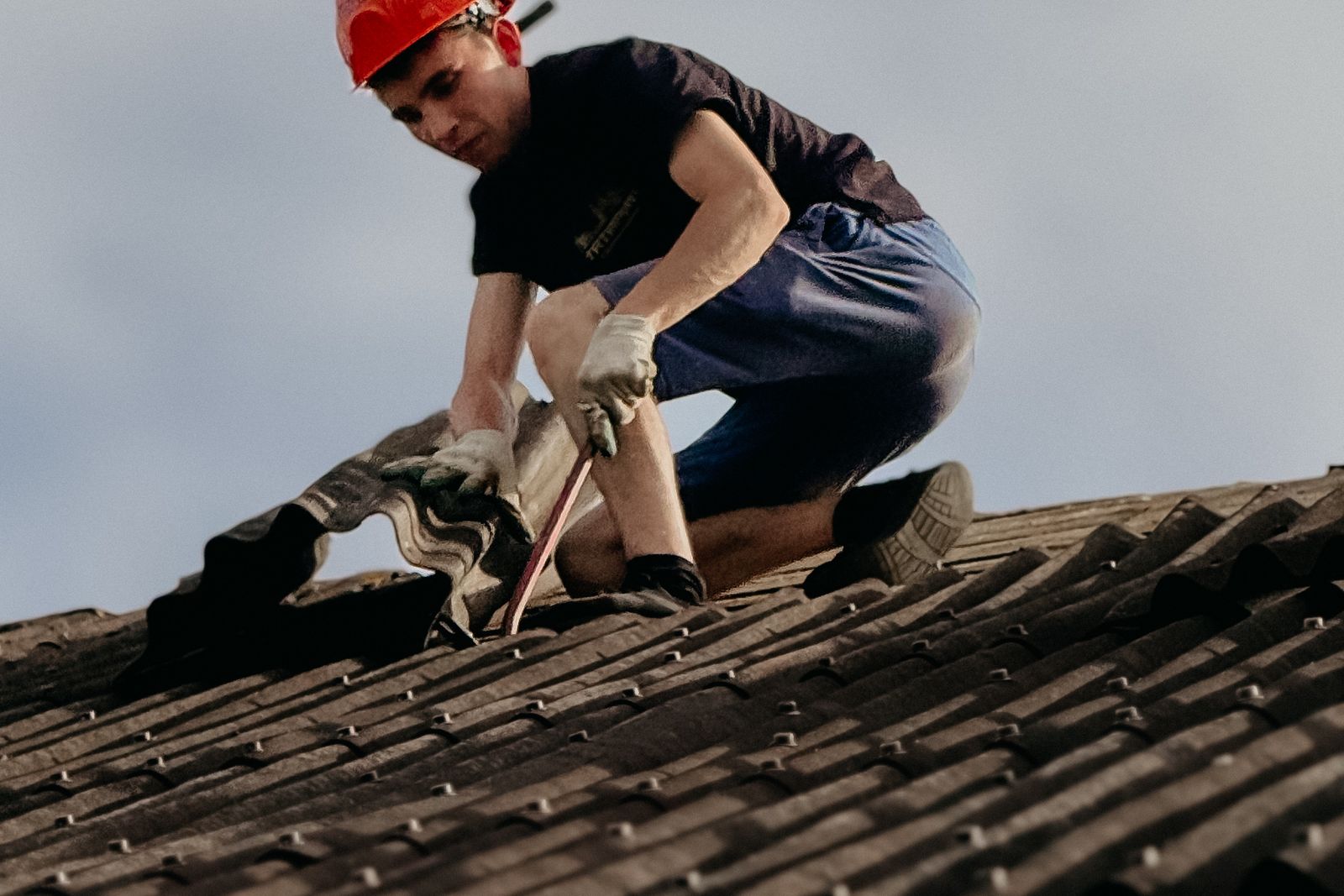 Roofer in a hard hat replacing a tile on a pitched roof