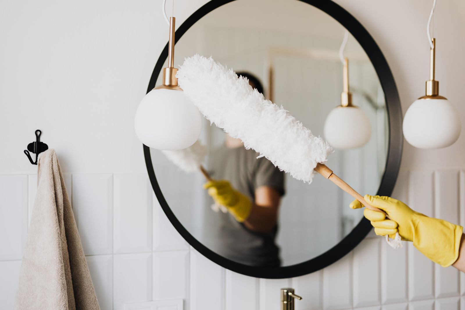 Cleaner dusting a round bathroom mirror with a soft duster