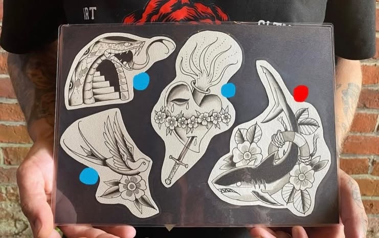 Hand-painted flash sheet of snake, sacred heart, swallow and shark designs held up at the studio
