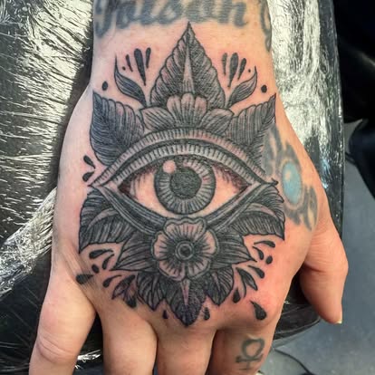 All-seeing eye and floral ornamental tattoo in black and grey on the back of a hand