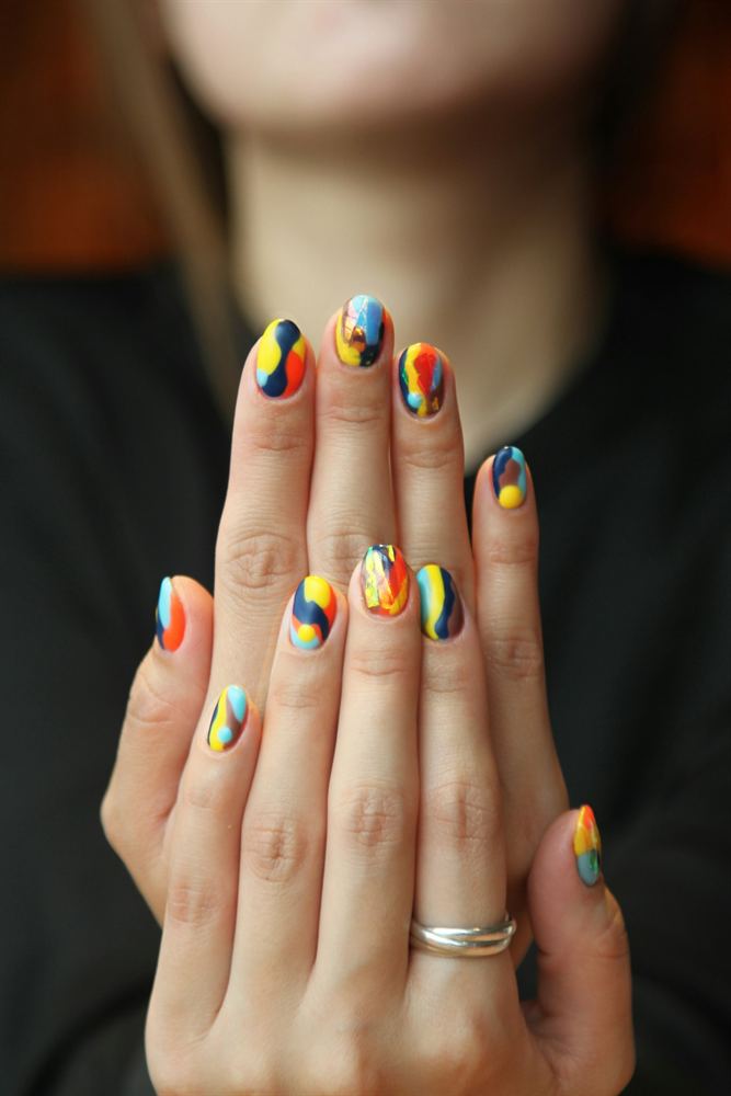 Short round nails painted with bold multi-coloured abstract freehand designs