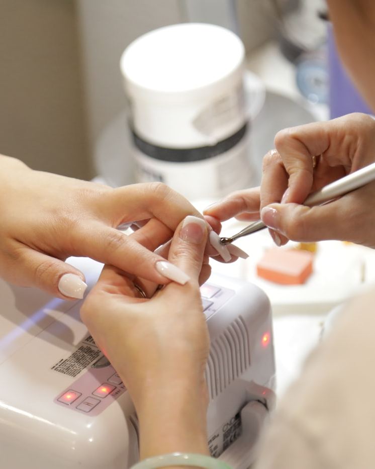 A nail technician shaping and applying gel polish to a client's nails at a salon workstation