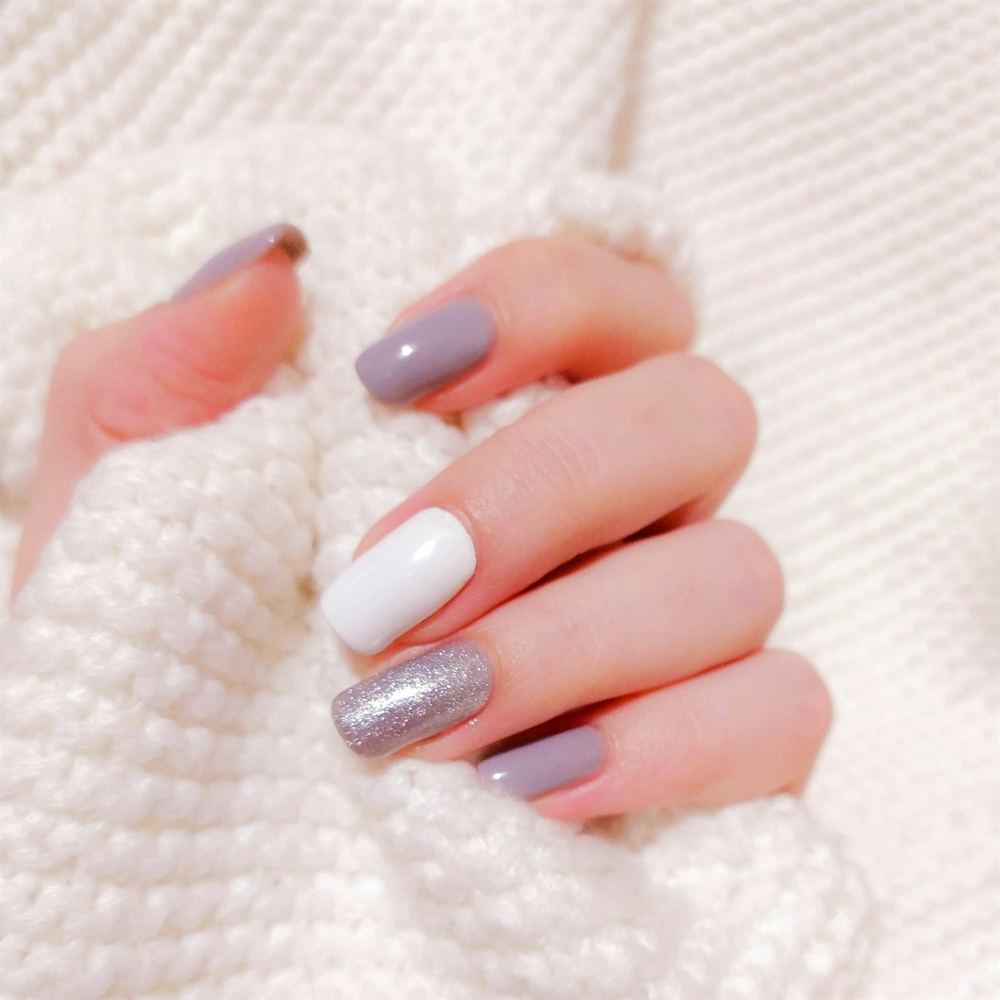 Square gel nails in grey, white and silver glitter against a cream knit