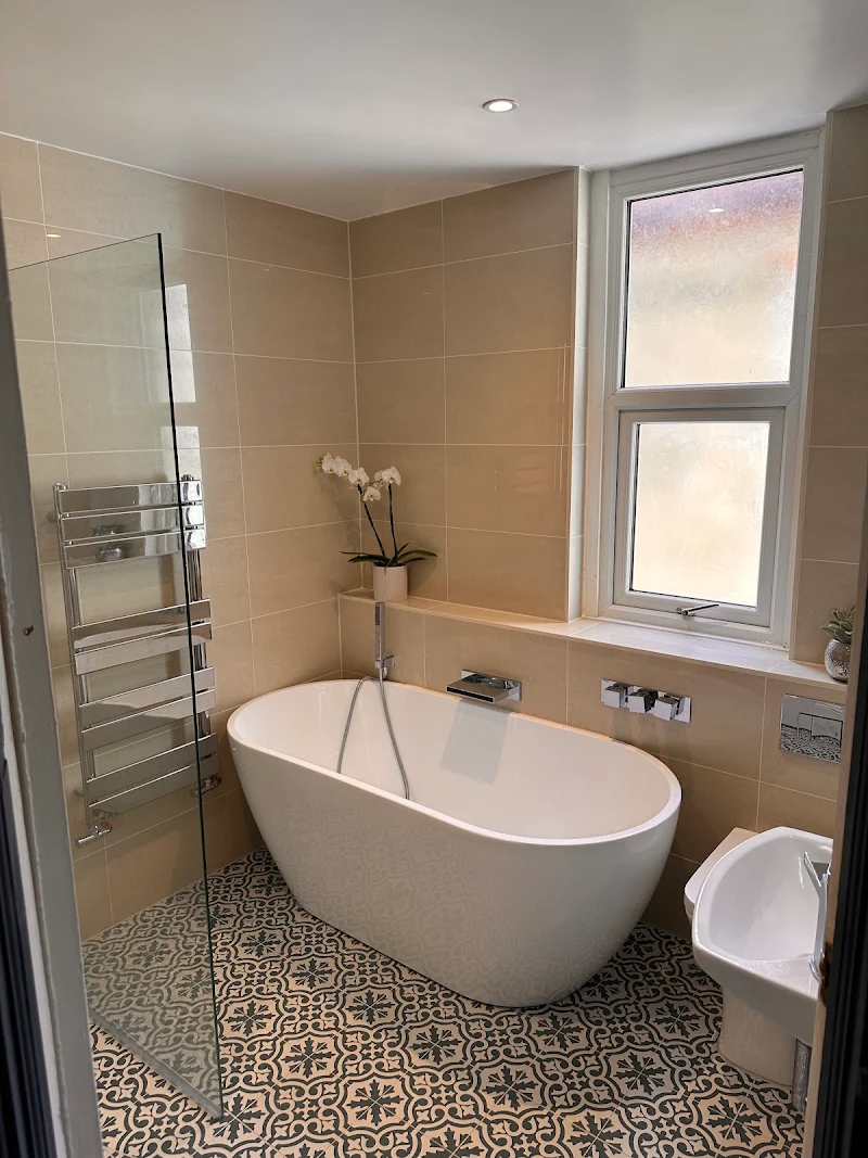 Finished bathroom by TJ Plumbing with freestanding bath, towel radiator and patterned floor tiles