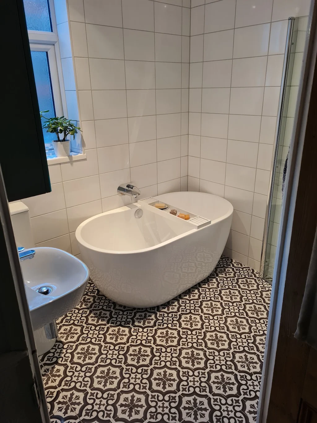 Freestanding bath with black tap on patterned floor tiles, fitted by TJ Plumbing