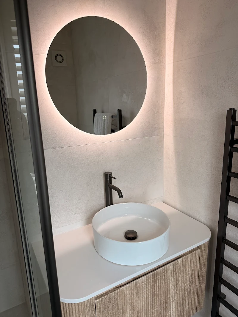 Countertop basin with black tap, wood vanity and backlit round mirror